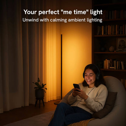 Young woman sitting in bean bag chair on phone in a room lit by the warm cozy glow of the floor lamp. 